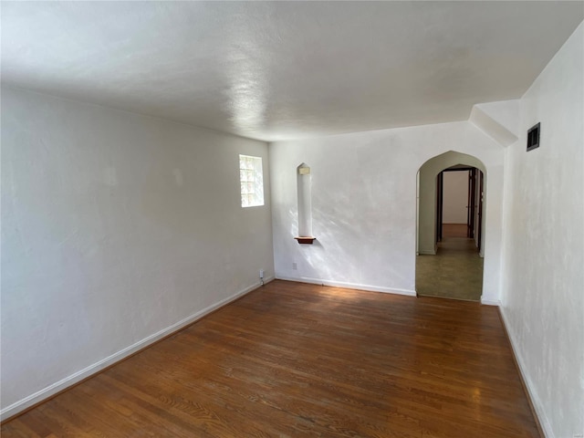 spare room featuring visible vents, arched walkways, baseboards, and wood finished floors