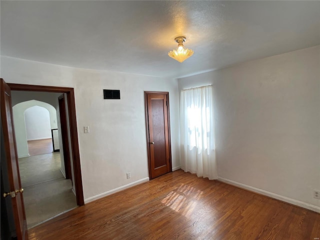 unfurnished bedroom featuring wood finished floors, visible vents, arched walkways, and baseboards