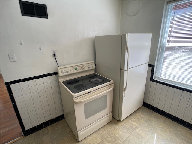 kitchen featuring white appliances, tile walls, and wainscoting