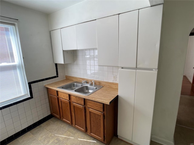 kitchen featuring tile walls, light countertops, brown cabinetry, white cabinetry, and a sink