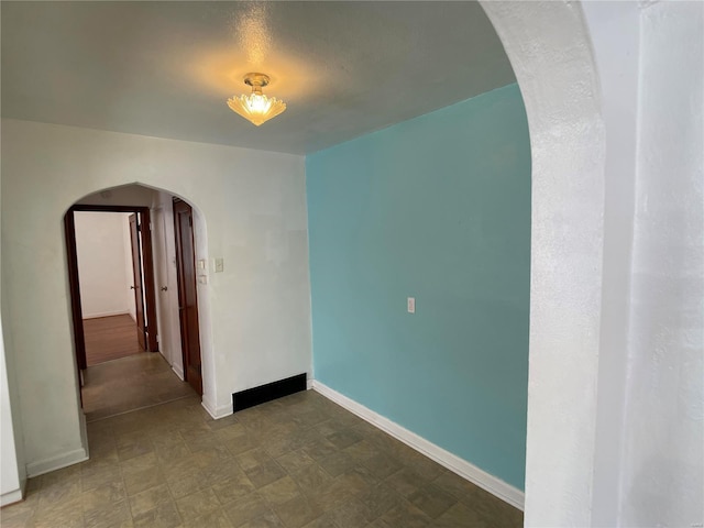 spare room featuring arched walkways and baseboards