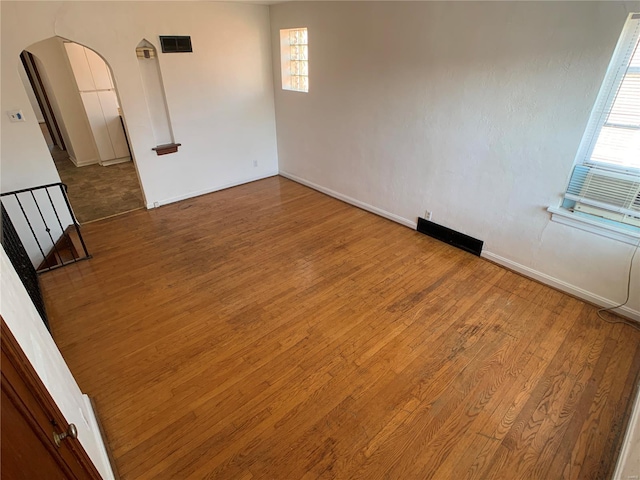 empty room featuring arched walkways, visible vents, a healthy amount of sunlight, and wood finished floors