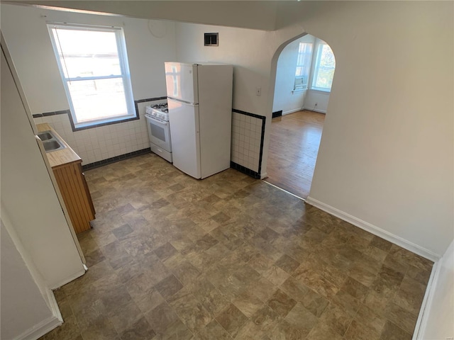 kitchen featuring a sink, white appliances, arched walkways, tile walls, and light countertops