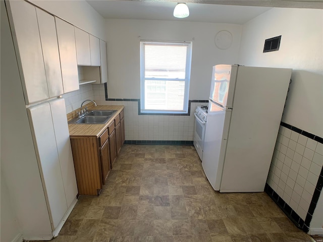 kitchen featuring a sink, white appliances, tile walls, and light countertops