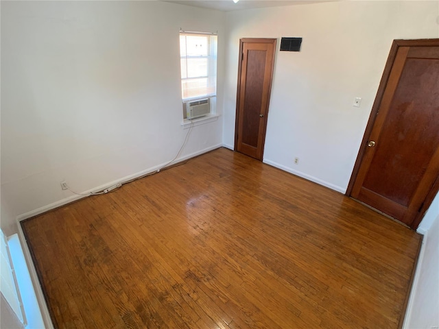 spare room featuring baseboards, wood-type flooring, visible vents, and cooling unit