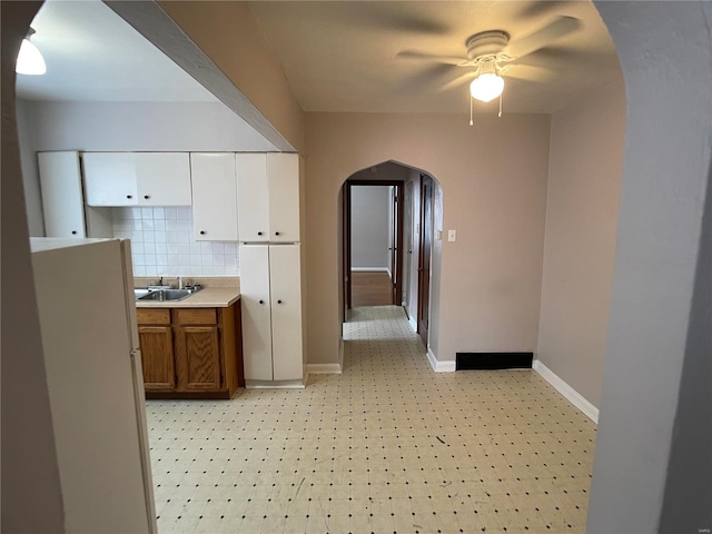 hallway featuring a sink, baseboards, arched walkways, and light floors