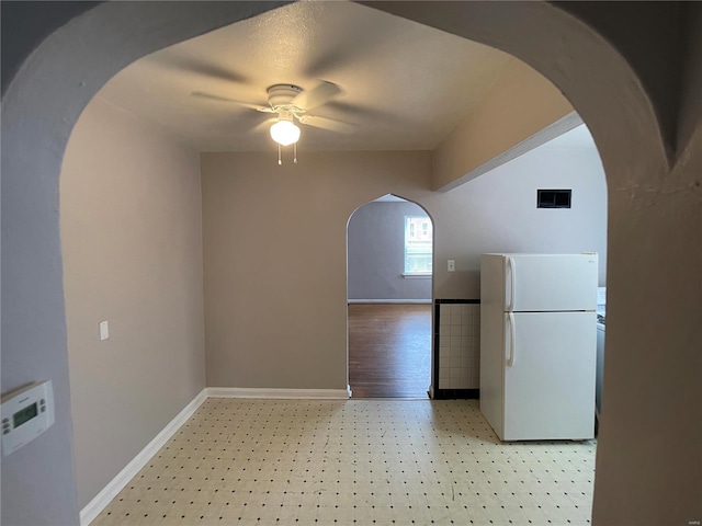 interior space featuring baseboards, light floors, arched walkways, and ceiling fan