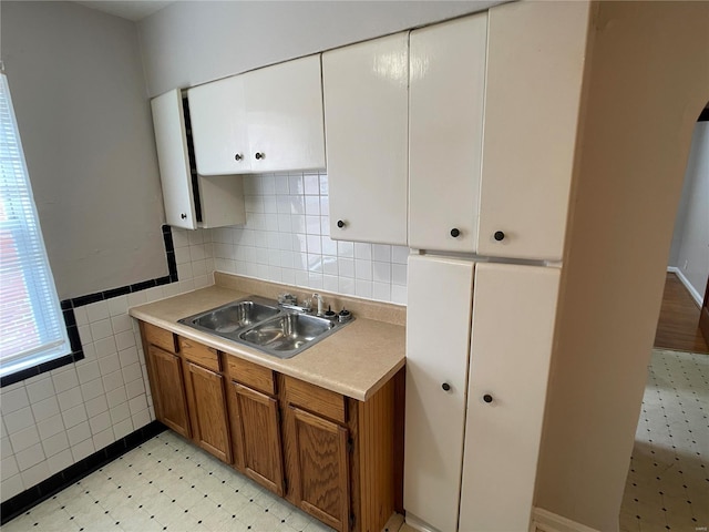 kitchen featuring brown cabinetry, a sink, light countertops, white cabinets, and tile walls