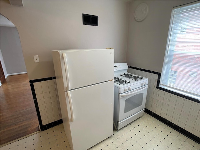 kitchen featuring white appliances, arched walkways, light floors, and tile walls