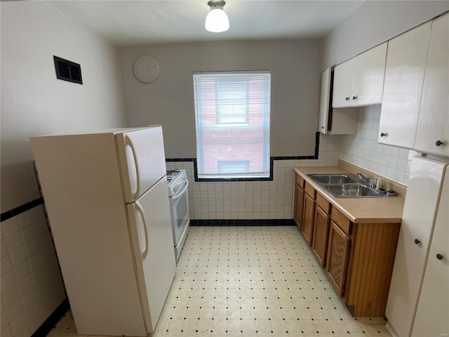 kitchen featuring a sink, white appliances, tile walls, brown cabinetry, and light floors