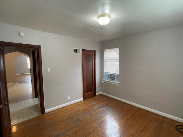 empty room with cooling unit, wood finished floors, visible vents, baseboards, and arched walkways