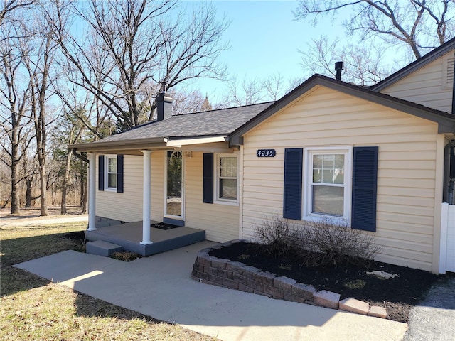 bungalow-style home with covered porch, a chimney, and a shingled roof