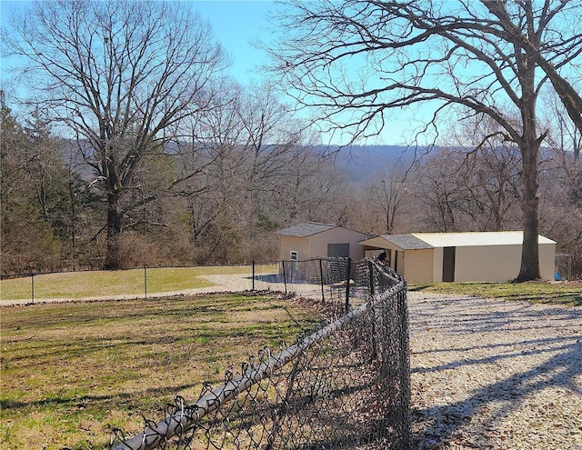 view of yard with an outbuilding, a wooded view, and fence