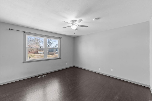 spare room with visible vents, a ceiling fan, dark wood-type flooring, and baseboards