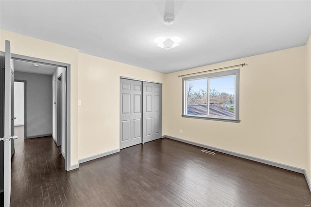 unfurnished bedroom with dark wood finished floors, visible vents, baseboards, and a closet