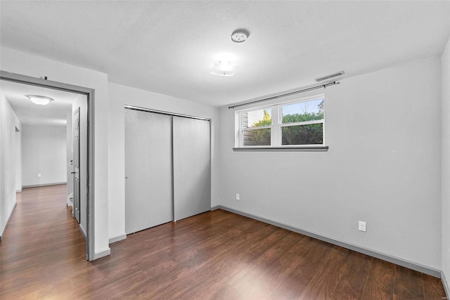 unfurnished bedroom featuring visible vents, a textured ceiling, wood finished floors, a closet, and baseboards