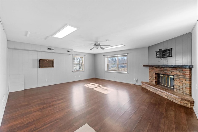 unfurnished living room featuring visible vents, a brick fireplace, ceiling fan, and wood finished floors