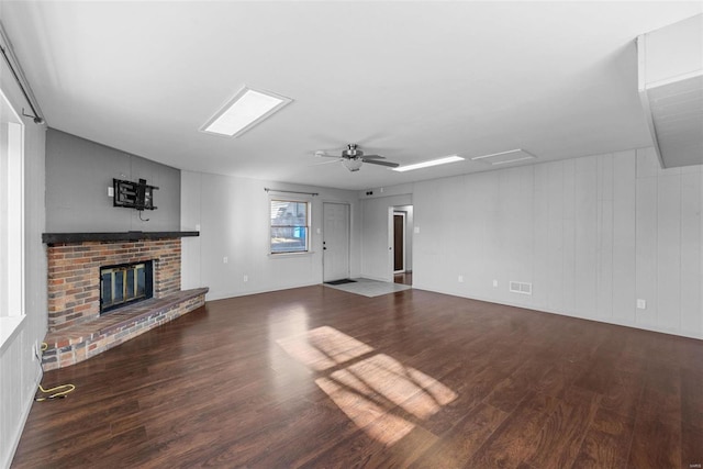 unfurnished living room with visible vents, a brick fireplace, a ceiling fan, and wood finished floors