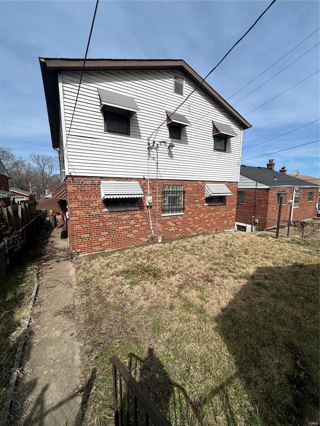 rear view of property with a lawn, brick siding, and fence