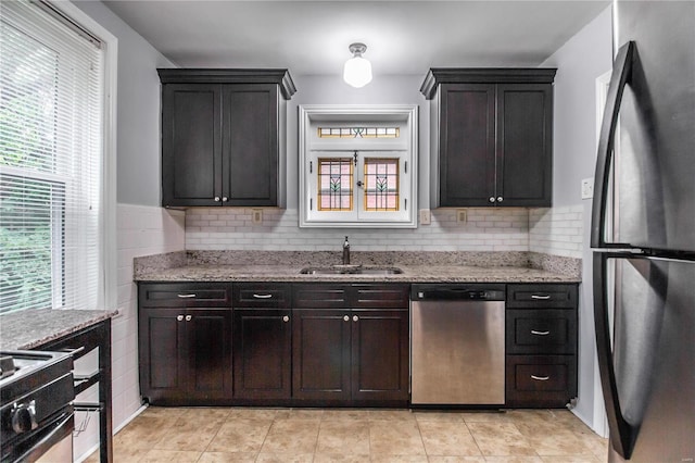 kitchen featuring a wealth of natural light, light stone countertops, appliances with stainless steel finishes, and a sink