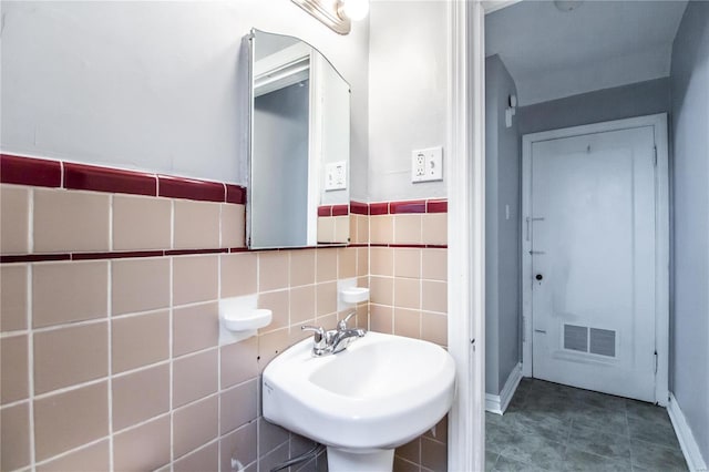 bathroom featuring a sink, visible vents, tile walls, and a wainscoted wall