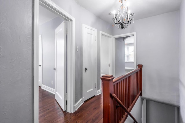 corridor with an inviting chandelier, an upstairs landing, wood finished floors, and baseboards