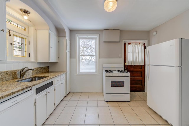 kitchen featuring light tile patterned floors, wainscoting, white appliances, and a sink