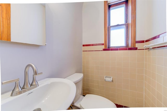 half bathroom with tile walls, toilet, wainscoting, and a sink