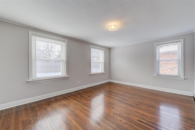 empty room featuring dark wood-type flooring, crown molding, and baseboards