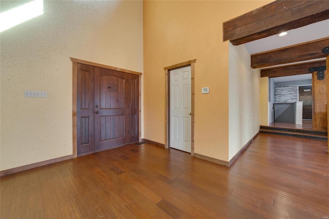 empty room with a textured wall, beamed ceiling, baseboards, and wood finished floors