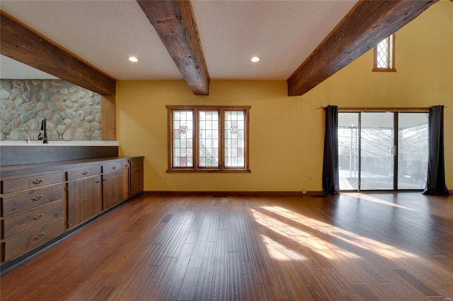 unfurnished living room with beamed ceiling, wood finished floors, and baseboards