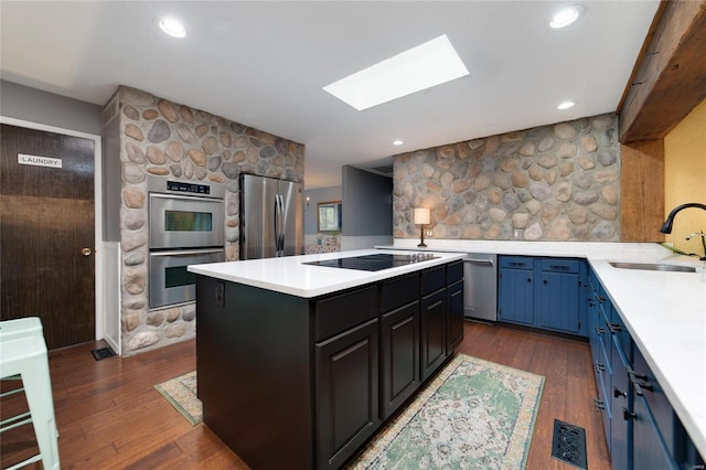 kitchen featuring dark wood-type flooring, a sink, stainless steel appliances, a skylight, and light countertops