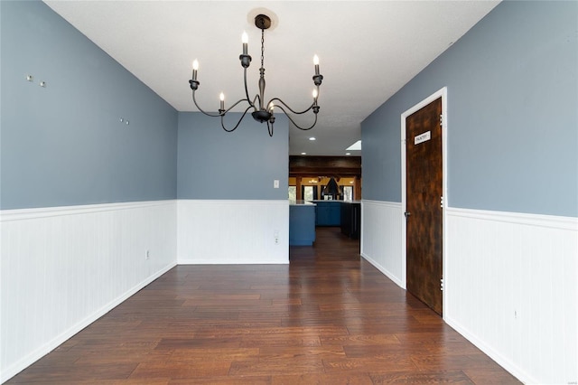 unfurnished dining area with dark wood-type flooring, a wainscoted wall, and a chandelier