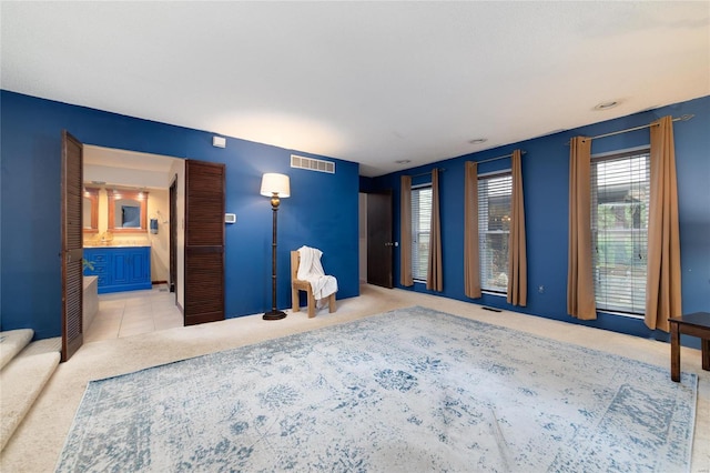 unfurnished bedroom featuring tile patterned flooring, visible vents, ensuite bathroom, and carpet