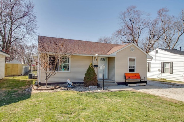 view of front of property with central air condition unit, a shingled roof, a front lawn, and fence