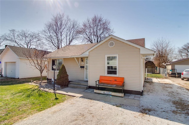 view of front of home featuring an outbuilding, a front yard, fence, roof with shingles, and a garage