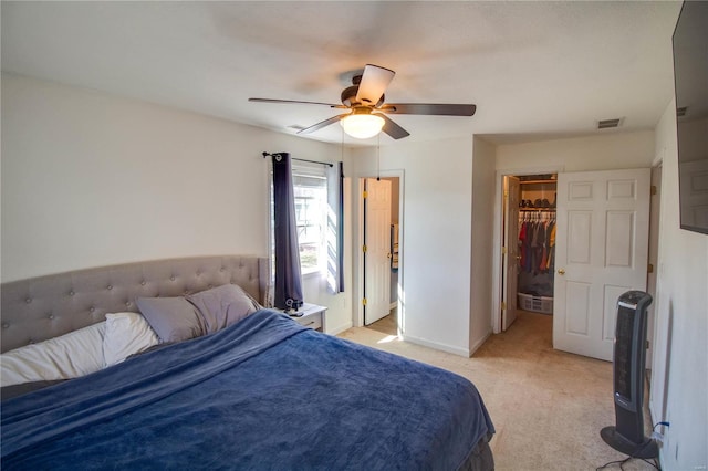 bedroom with visible vents, a walk in closet, baseboards, light colored carpet, and a ceiling fan