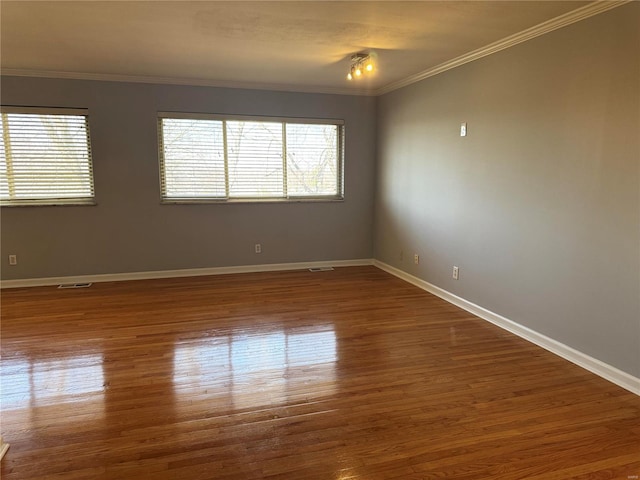 spare room featuring visible vents, baseboards, wood finished floors, and crown molding