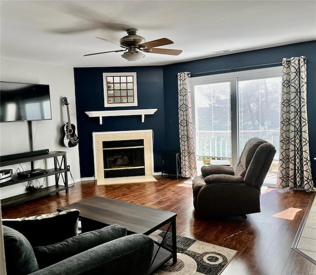 living room with a glass covered fireplace, wood finished floors, a ceiling fan, and visible vents