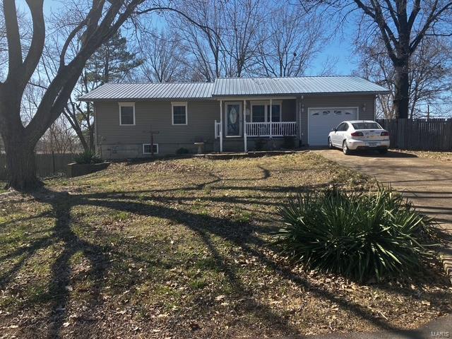 view of front of property with fence, covered porch, concrete driveway, a garage, and metal roof