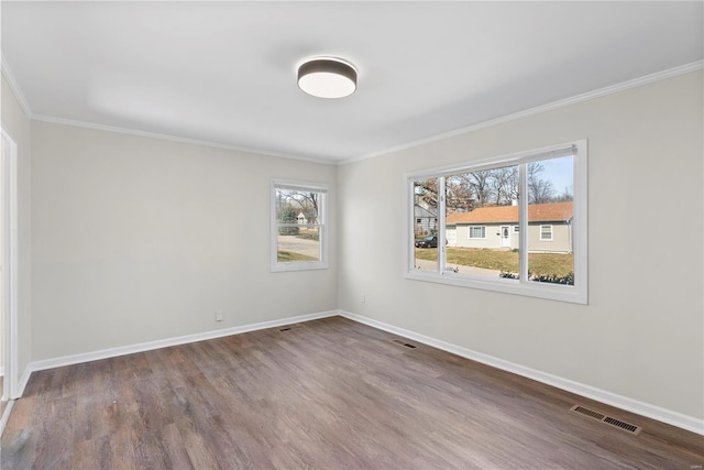 spare room featuring wood finished floors, baseboards, visible vents, and ornamental molding