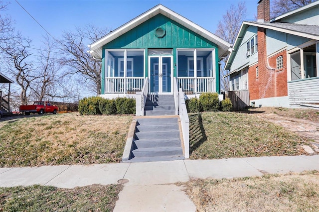 bungalow featuring french doors, a front yard, stairs, and a sunroom