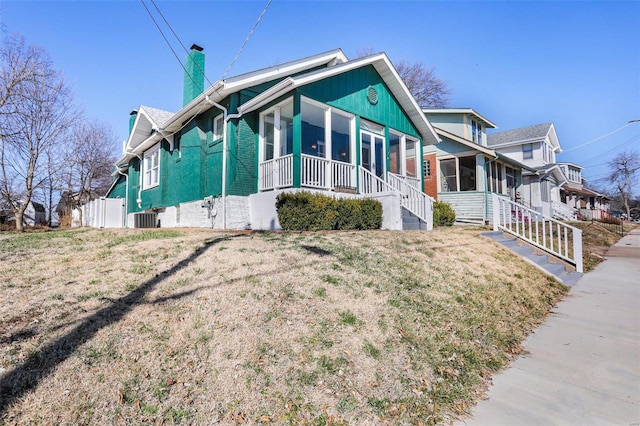 view of side of home with a yard, covered porch, central AC, and a chimney