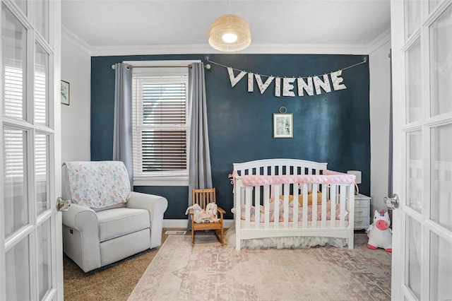 carpeted bedroom with an accent wall, baseboards, ornamental molding, french doors, and a nursery area