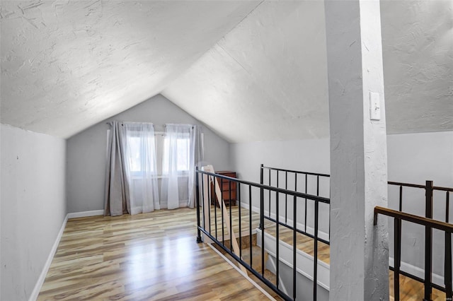 additional living space with baseboards, a textured ceiling, wood finished floors, and vaulted ceiling