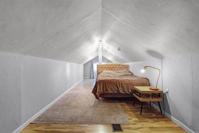 bedroom with wood finished floors, visible vents, baseboards, lofted ceiling, and a textured ceiling