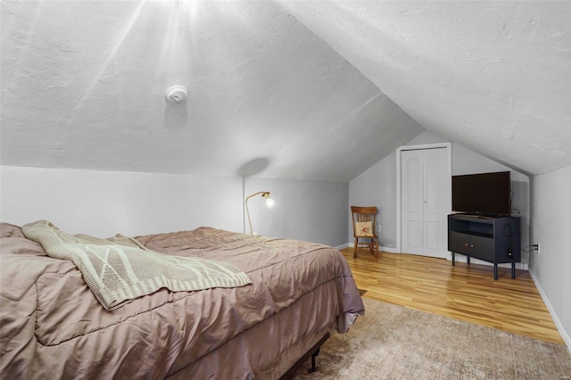 bedroom with baseboards, vaulted ceiling, wood finished floors, a closet, and a textured ceiling