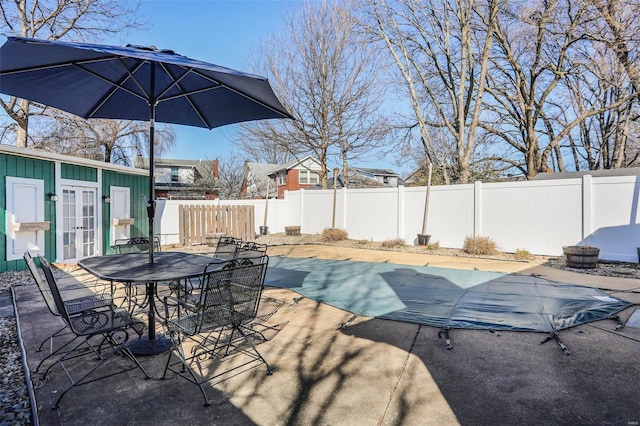 view of patio with outdoor dining space, a fenced backyard, a fenced in pool, and french doors