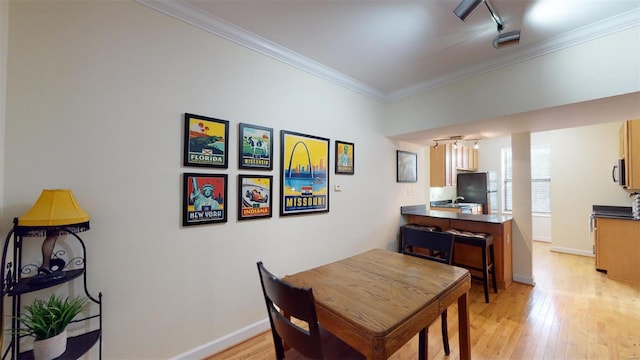 dining space with light wood finished floors, rail lighting, crown molding, and baseboards