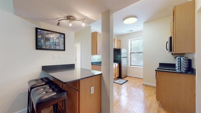 kitchen featuring appliances with stainless steel finishes, a breakfast bar area, a peninsula, light wood finished floors, and baseboards